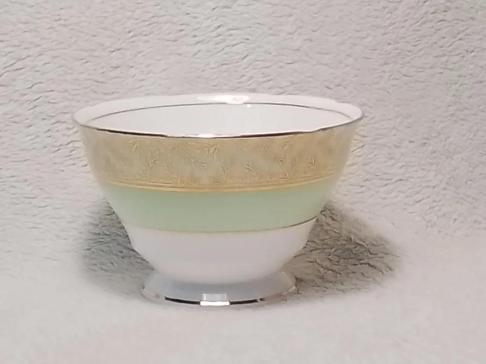 A decorative porcelain bowl with gold, pale green, and white sections, resting on a textured gray surface.