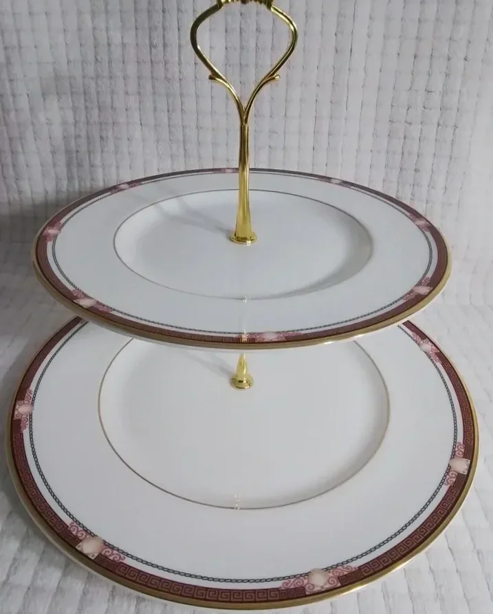 Two tiered decorative serving plates with gold accents and a central handle, set against a white background.
