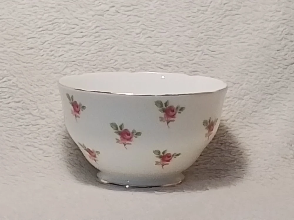 A white ceramic bowl with pink rose and green leaf pattern on the exterior, set against a textured off-white background.