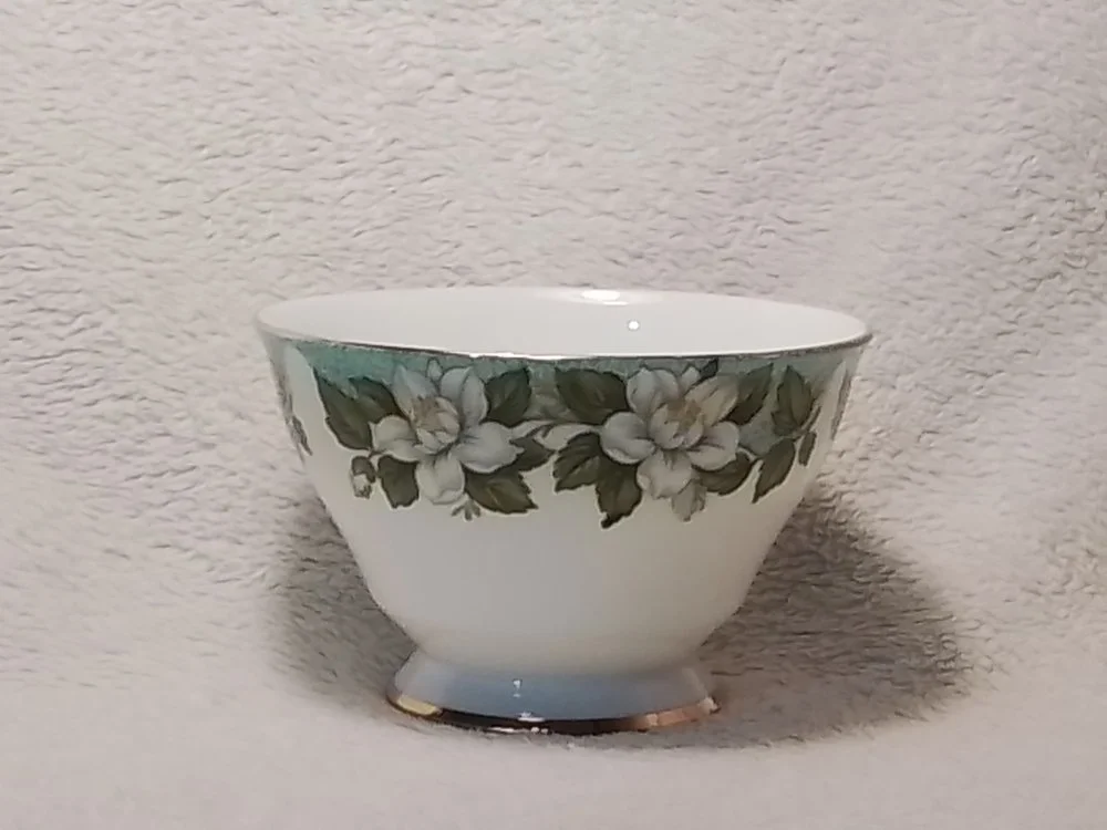 A white porcelain bowl with a floral pattern of white flowers and green leaves along the rim.