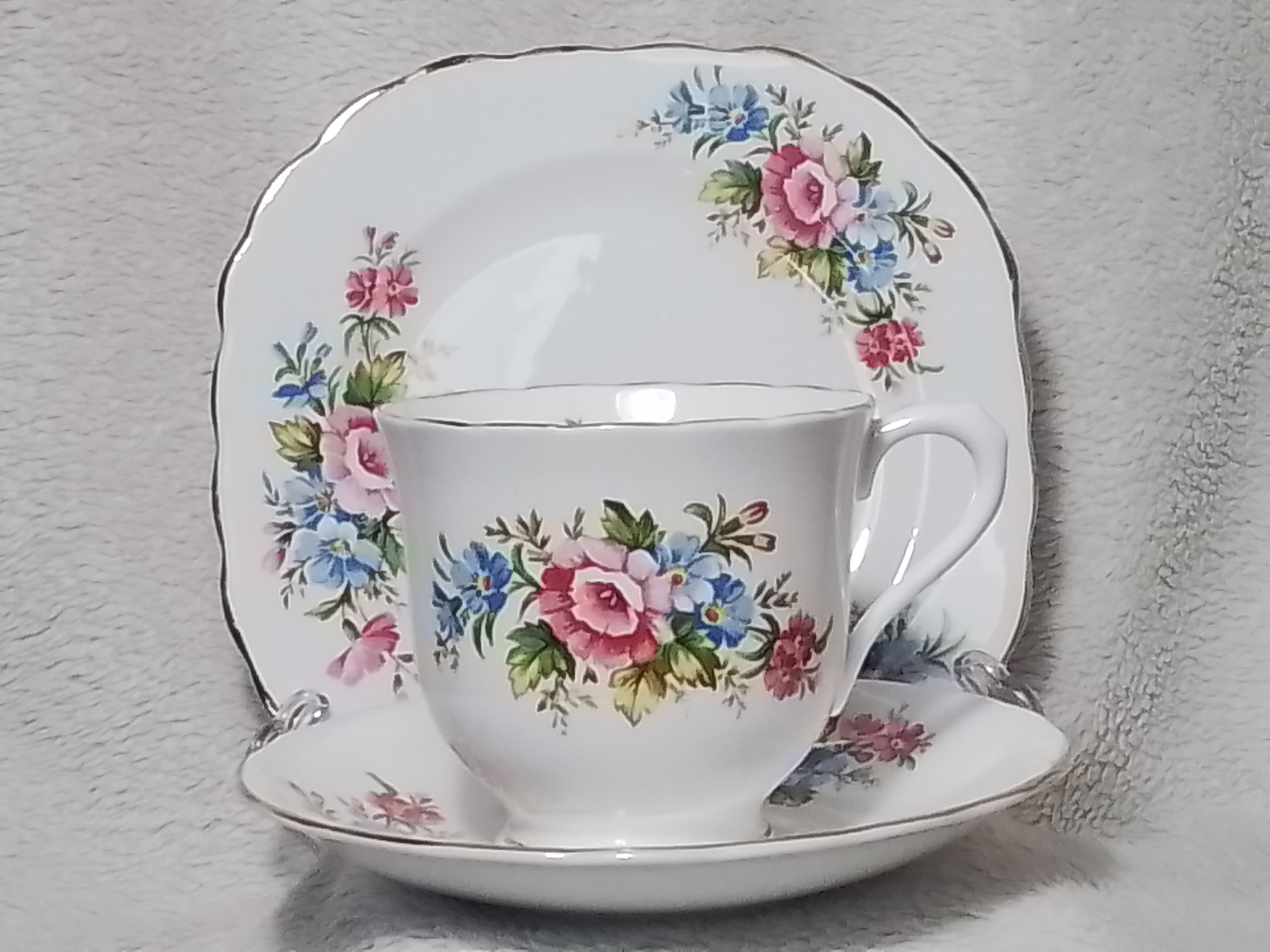 A floral patterned tea cup, saucer, and dessert plate with pink, blue, and green flowers on white ceramic.