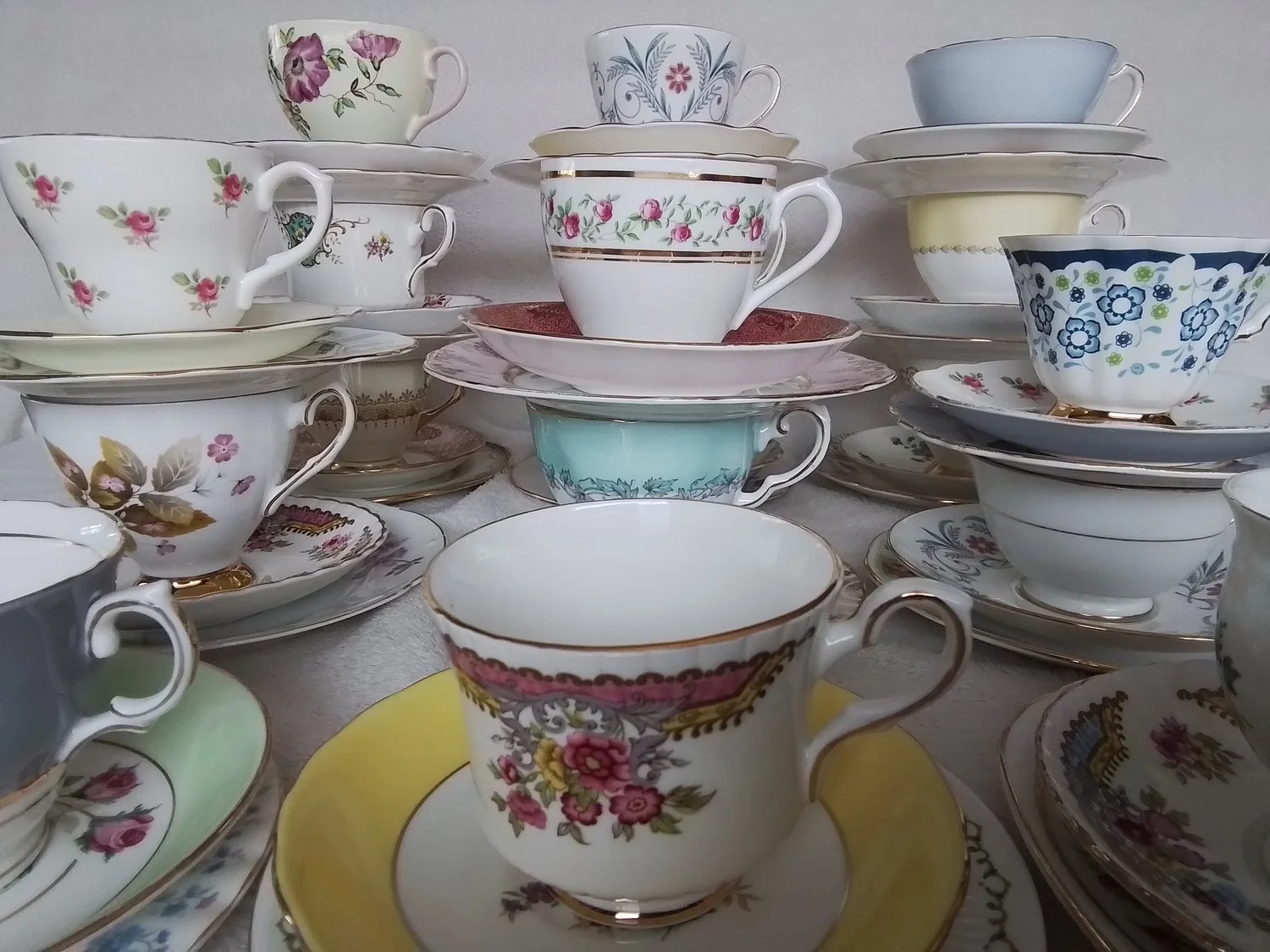 Collection of vintage teacups and saucers with floral patterns stacked on a surface.