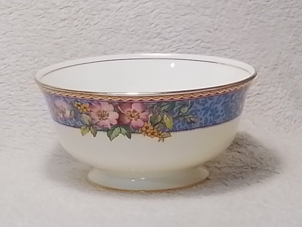 A porcelain bowl with floral design around the rim, including pink and purple flowers and green leaves, set against a light textured background.