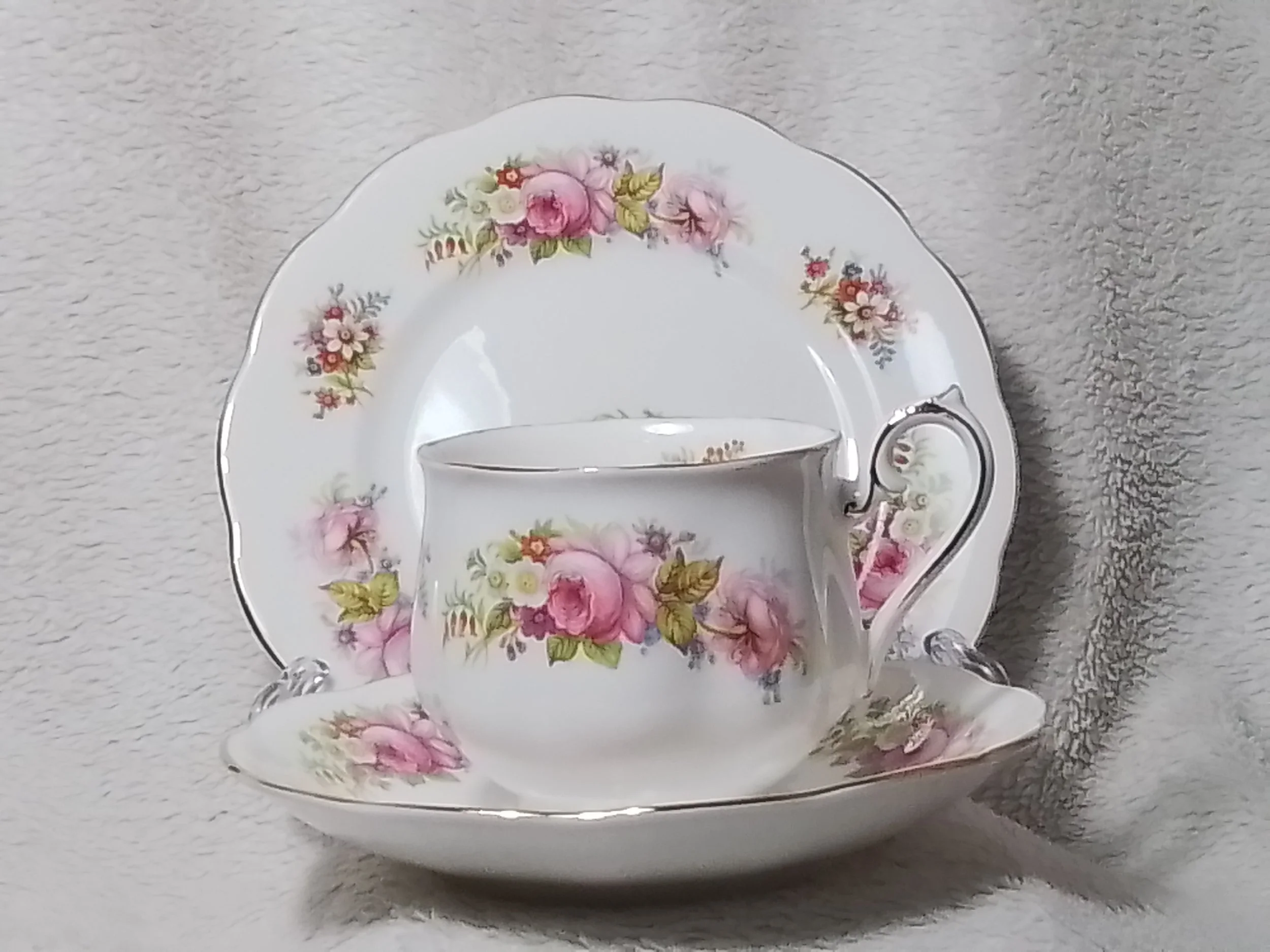 A porcelain teacup, saucer, and plate set with pink roses and floral patterns.