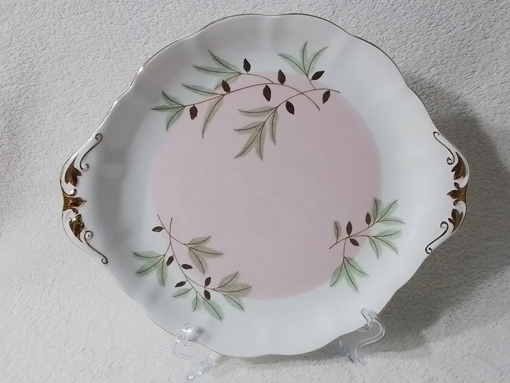 Decorative porcelain plate with a floral design in green, black, and gold, displayed on a clear stand.