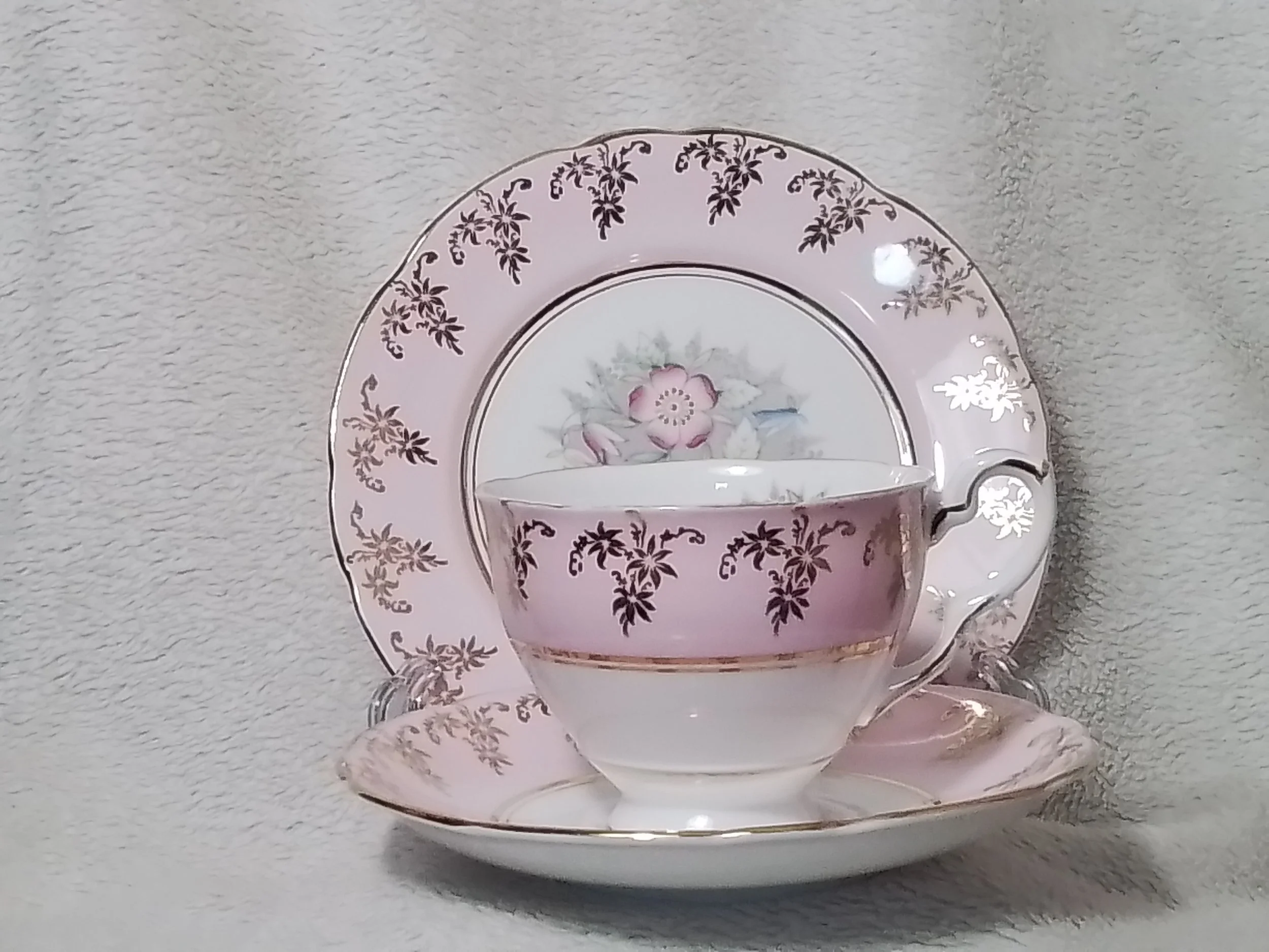 A pink floral patterned tea cup and saucer set with a matching plate in the background on a beige textured surface.