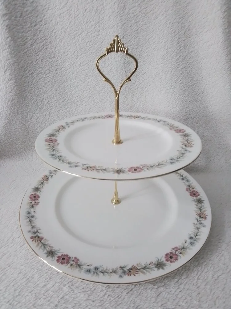 Two tiered porcelain serving tray with floral patterns and gold accents, placed against a textured gray background.