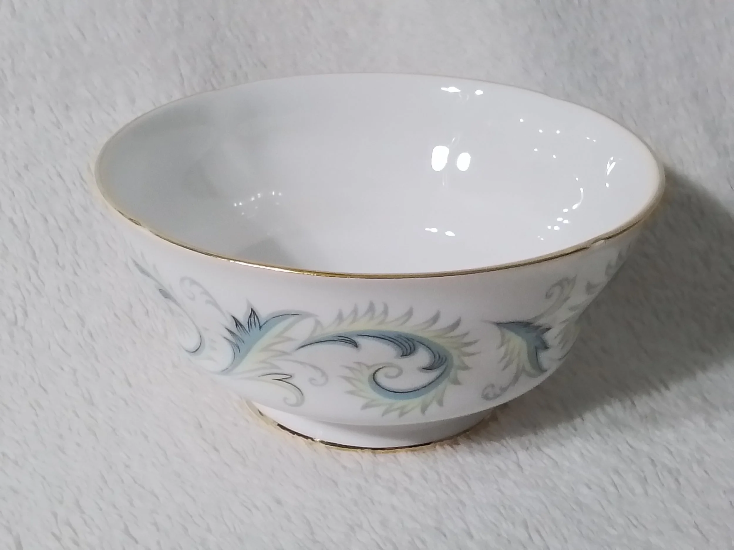 A white porcelain bowl with gold trim and light blue decorative swirls on its exterior