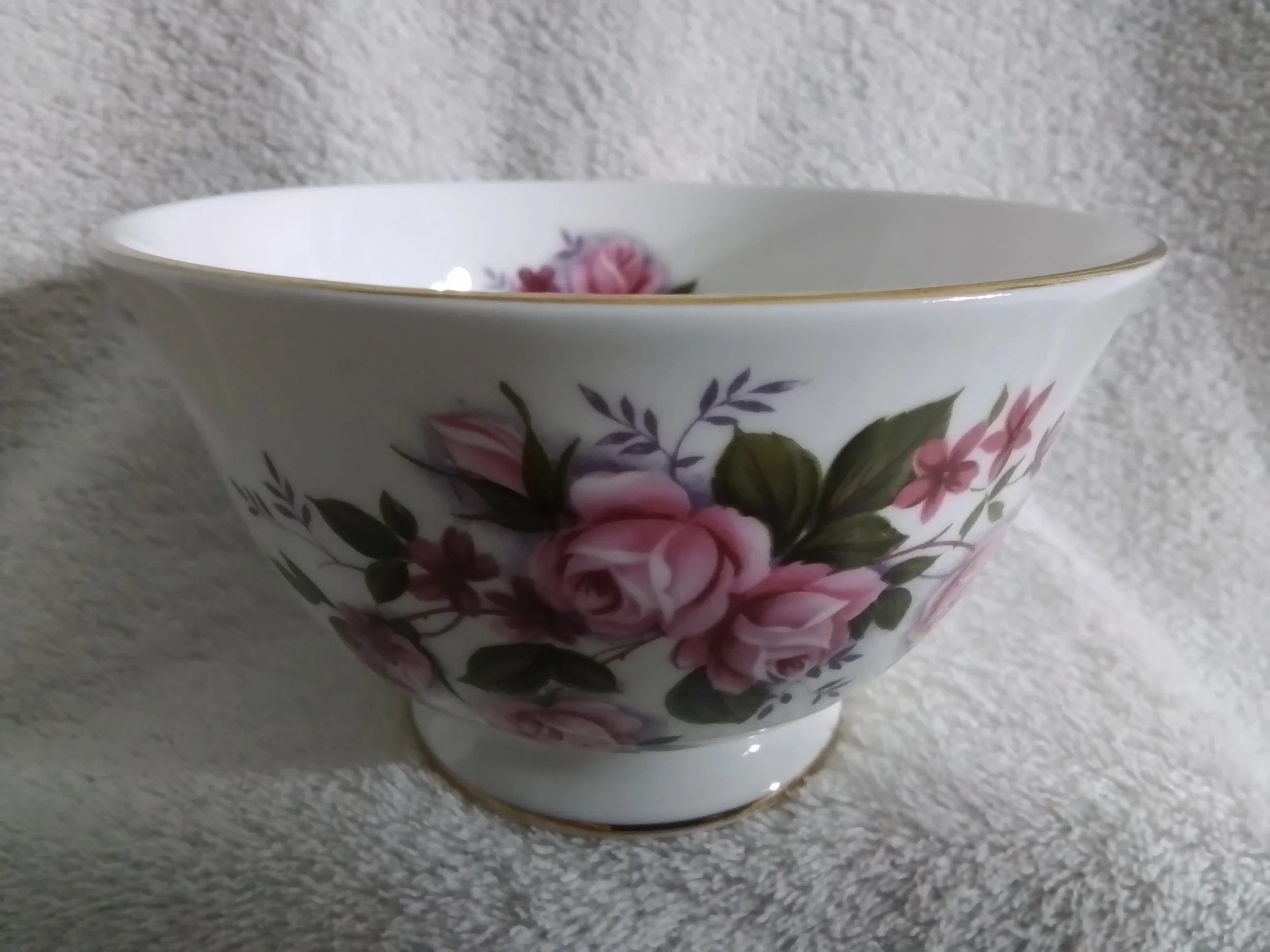 Porcelain bowl with pink floral pattern and gold trim, against a textured white background.