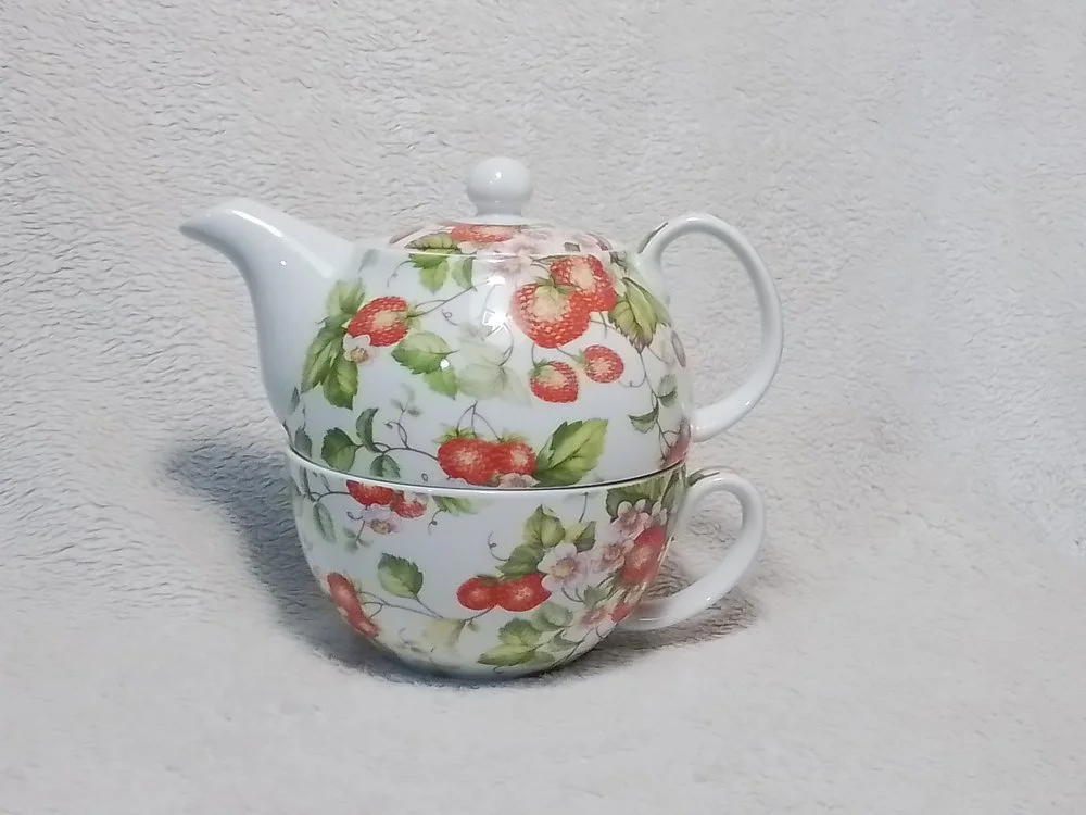 A teapot and a teacup stacked together, both with a strawberry and leaf pattern on a white background.
