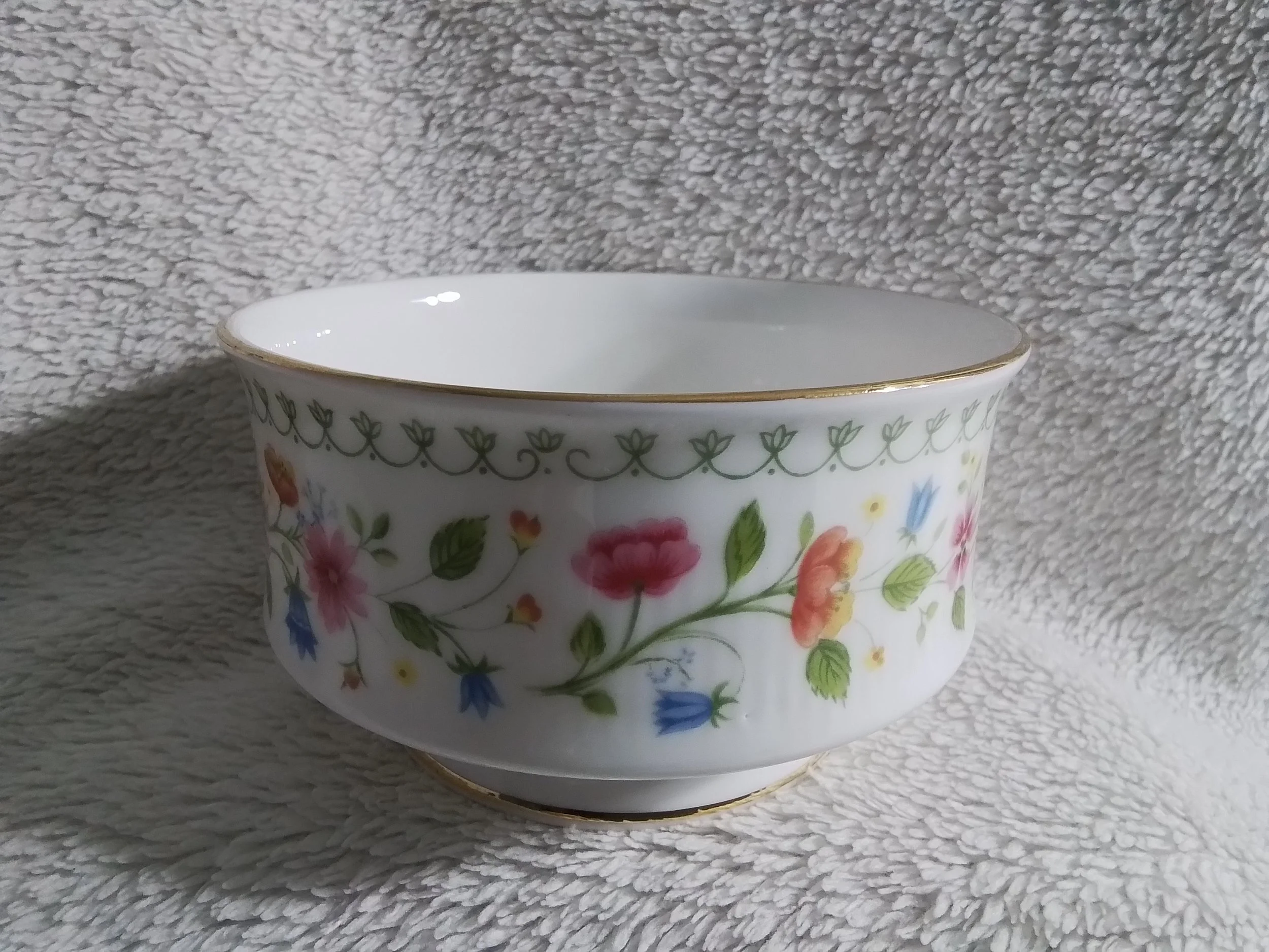 White porcelain bowl with floral pattern and gold rim, resting on a textured beige fabric background.