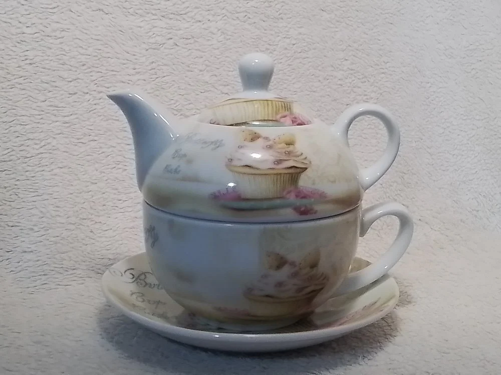 A porcelain tea set with a teapot, sugar bowl, and tray, all with floral patterns, placed against a textured beige background.