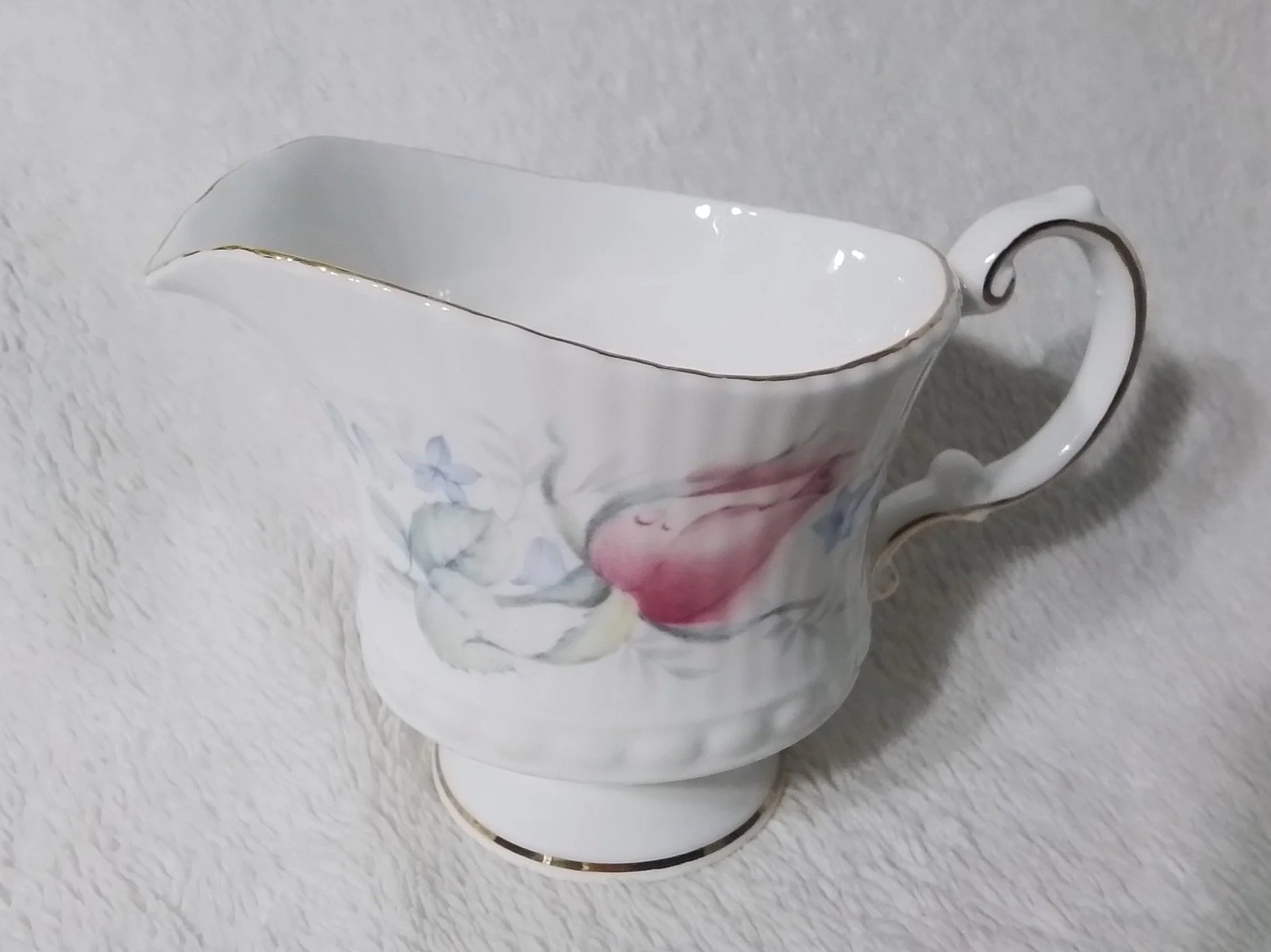 A white porcelain teacup with floral design and gold trim, positioned on a light-colored textured surface.