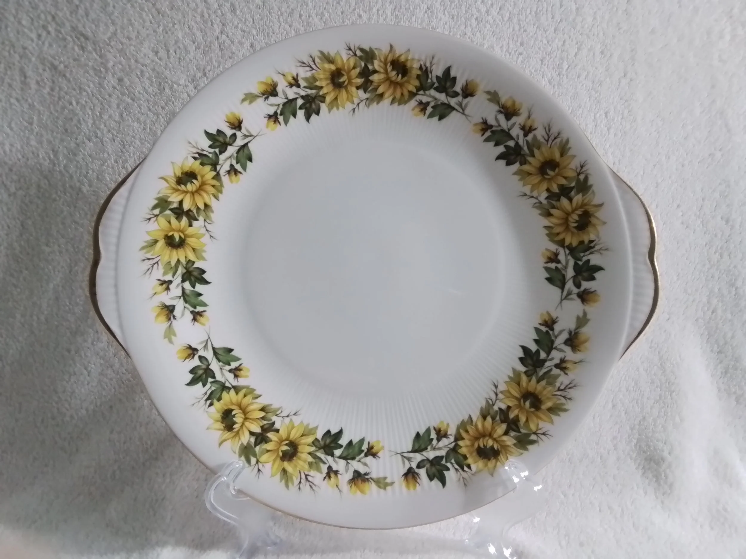 A white ceramic plate with a sunflower pattern border, gold rim, and scalloped edges, placed on a white textured surface.