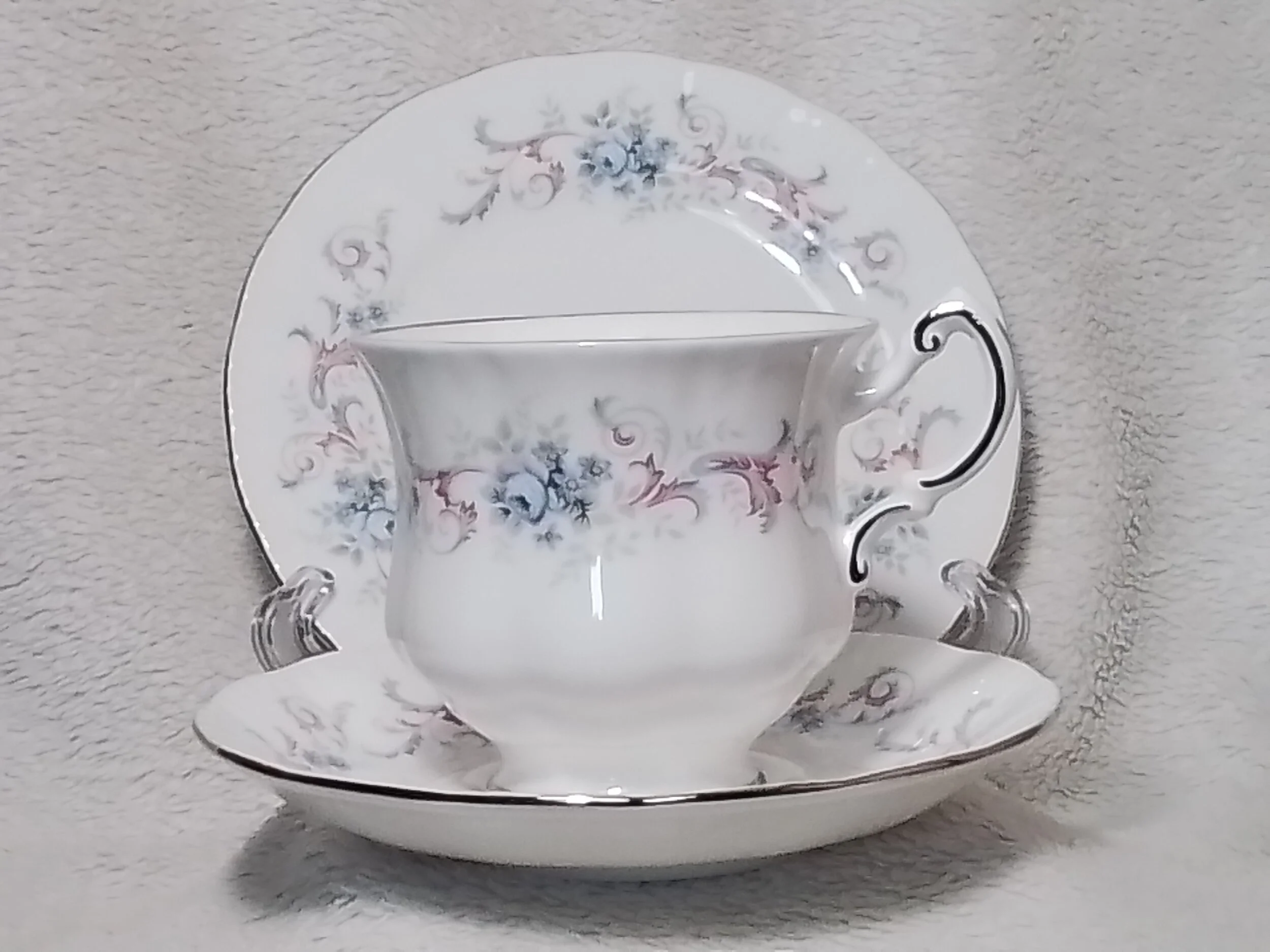 A porcelain teacup and saucer set with floral pattern, displayed on a stand against a light background.