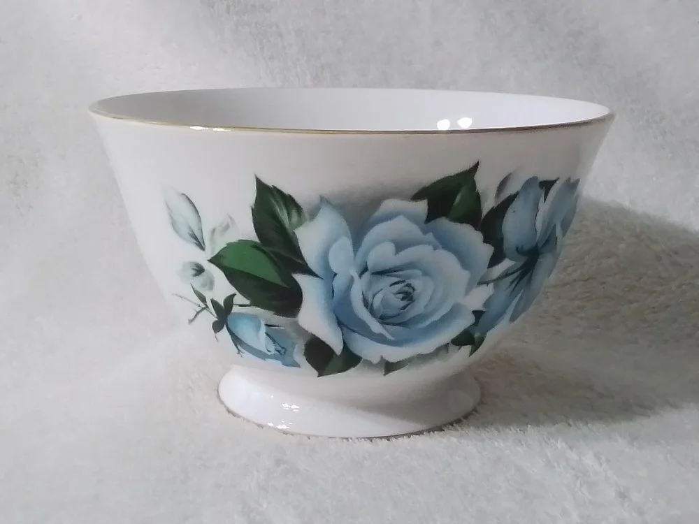 A white ceramic bowl with a floral pattern of blue roses and green leaves, placed on a light-colored surface.
