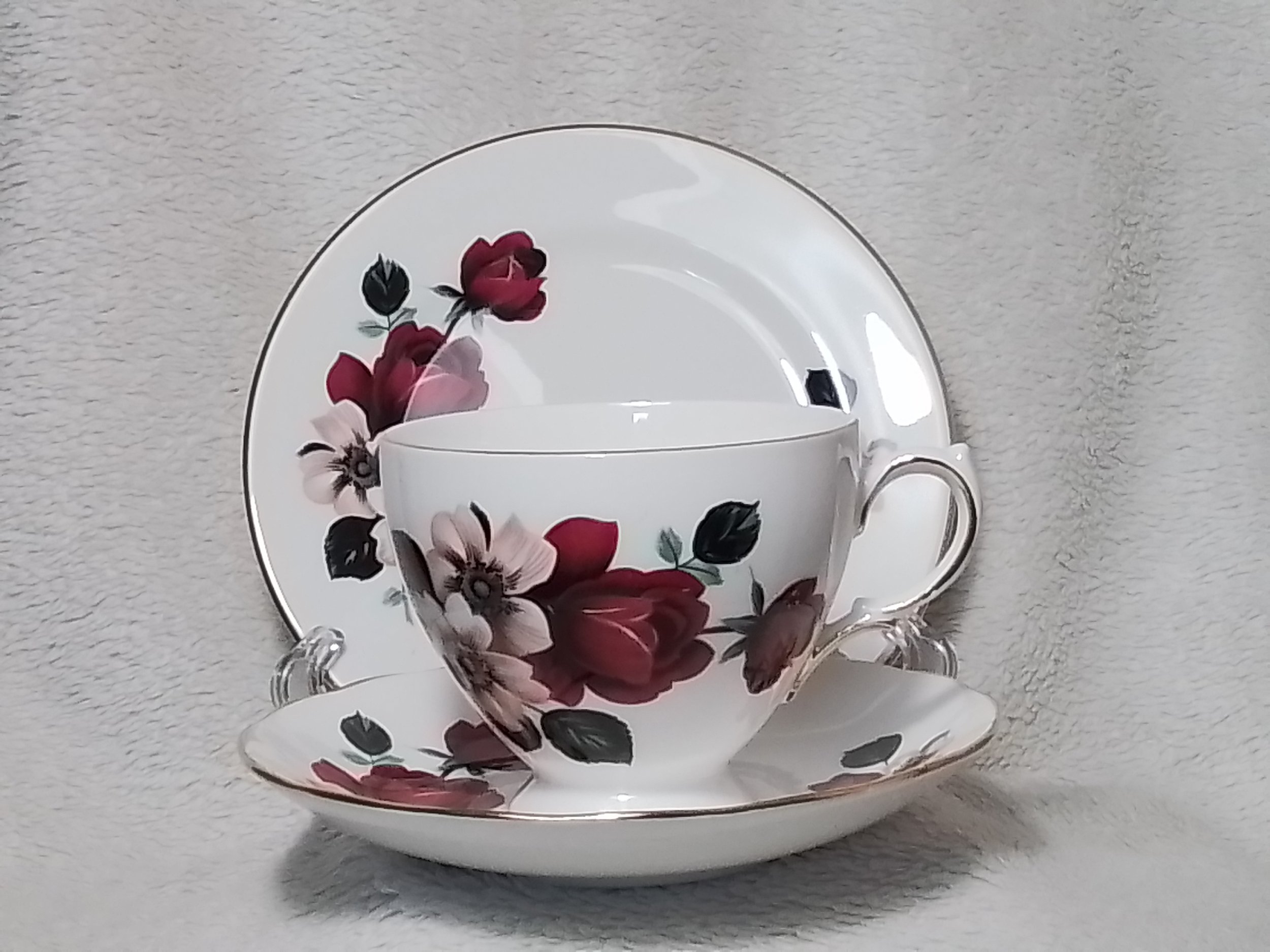 A white teacup with a floral pattern in red, pink, and black, placed on a matching saucer, against a light gray textured background.