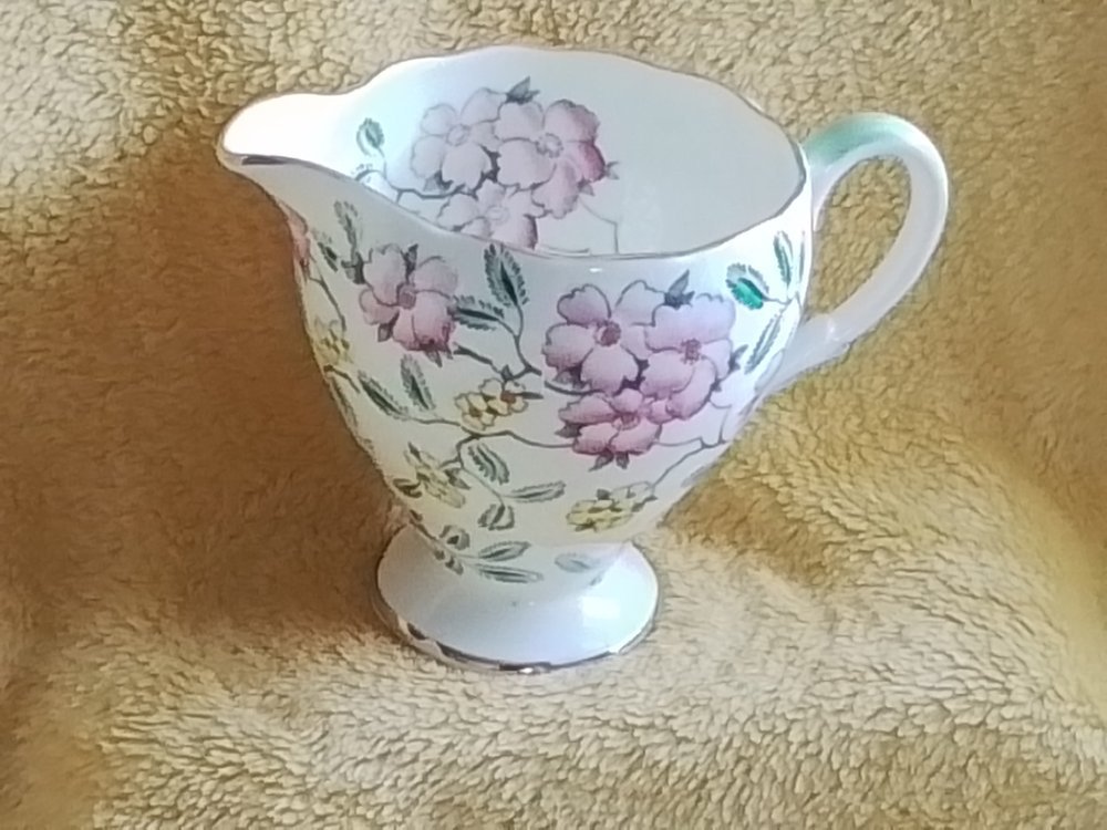 A decorative porcelain pitcher with a floral pattern, featuring pink and purple flowers and green leaves, placed against a textured yellow background.