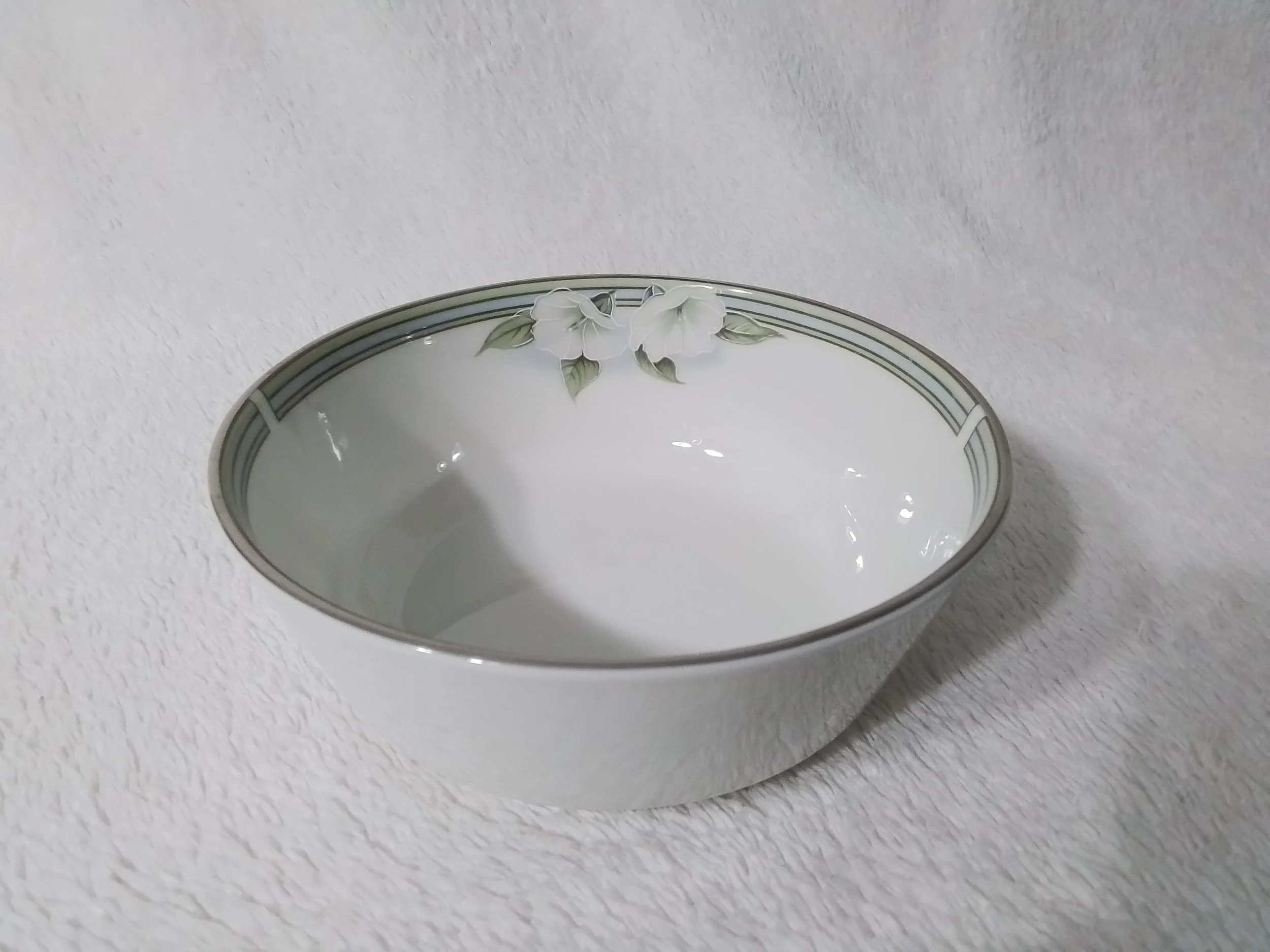 A white ceramic bowl with a floral design around the rim, featuring white flowers and green leaves, placed on a white textured surface.