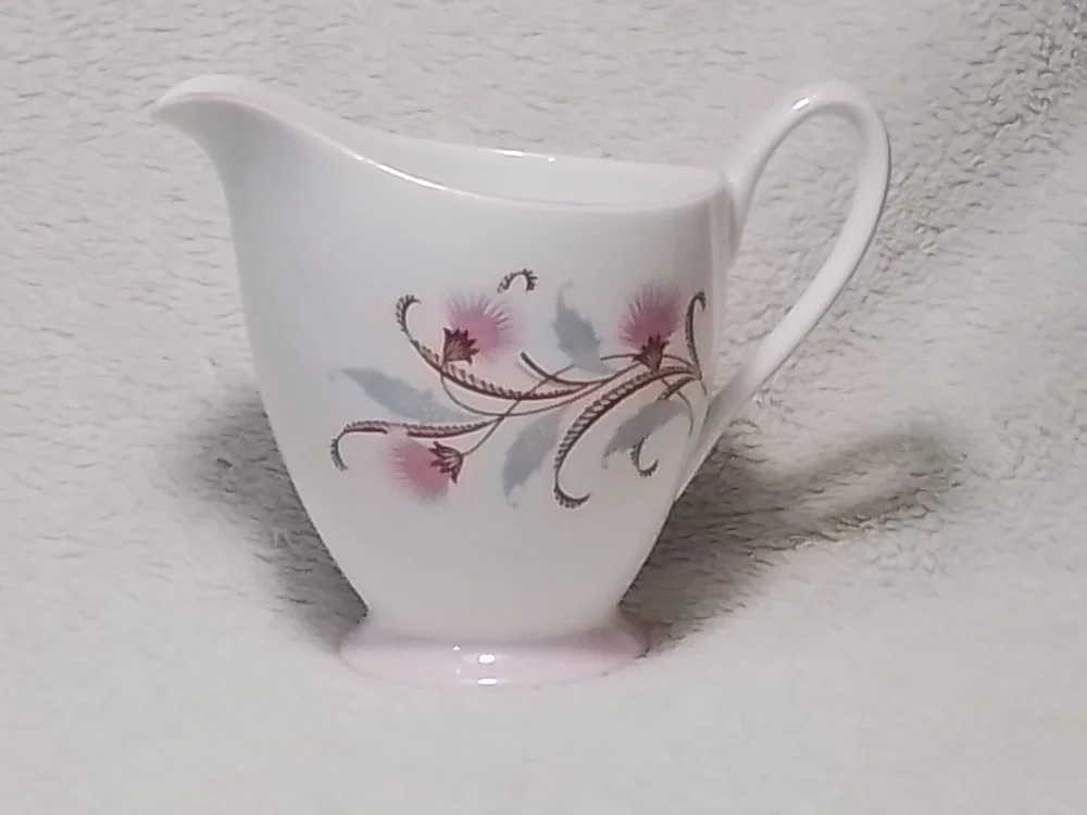 A white ceramic gravy boat with a floral pattern of pink flowers and brown vines.
