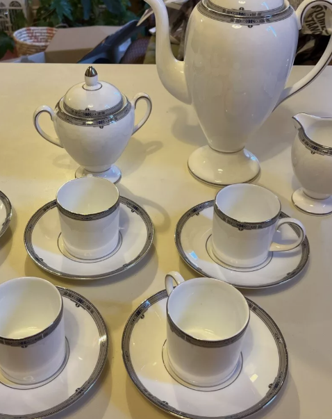 White porcelain tea set with silver trim, including a teapot, sugar bowl, creamer, and four cups with matching saucers, arranged on a table.