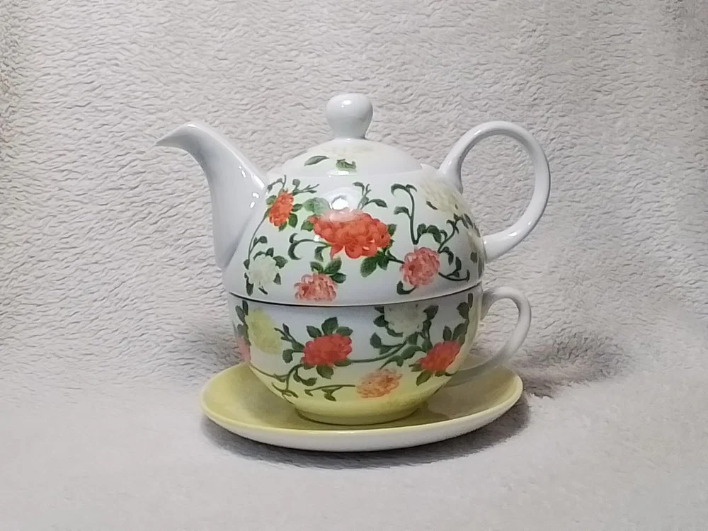 A porcelain teapot with a floral pattern on a matching cup and saucer, set against a textured light background.