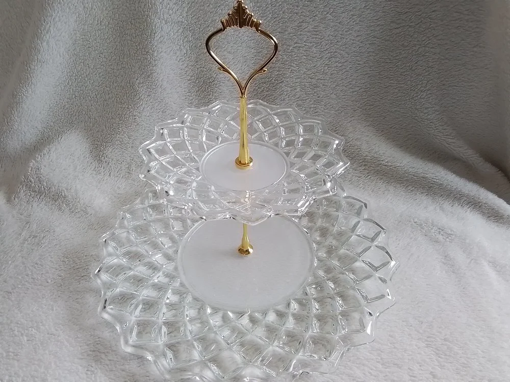 Three clear glass tiered serving trays with gold handles on a white textured surface.