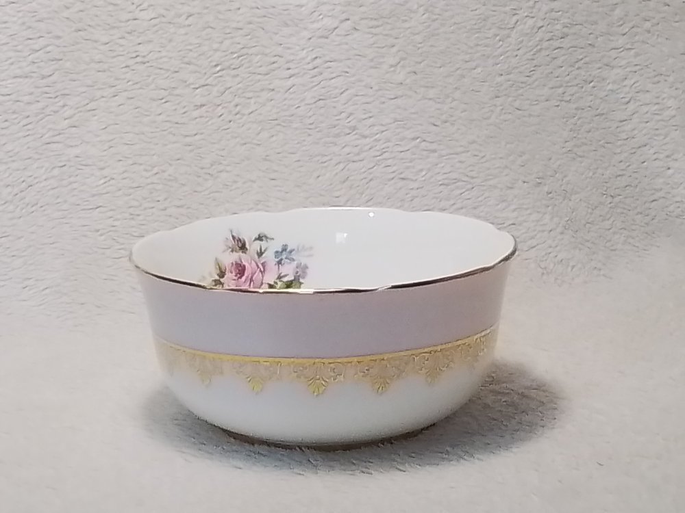 A white porcelain bowl with gold decorative trim and floral design on the inside. The bowl is placed on a textured surface.