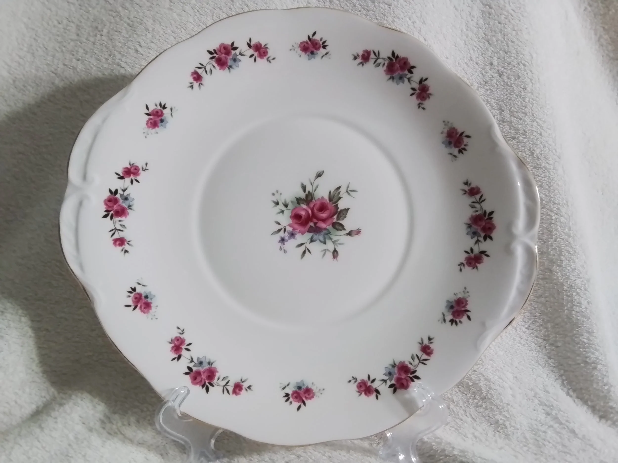 A white porcelain plate with pink and purple floral patterns on the rims and center, resting on a clear stand.