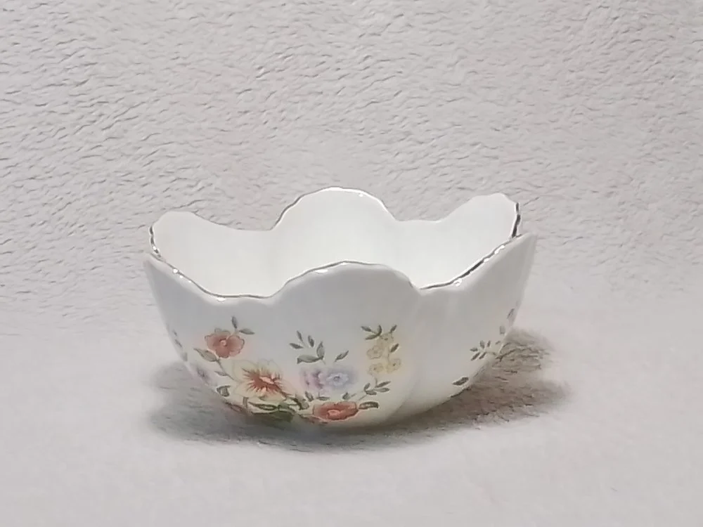 A small, decorative, floral-patterned porcelain bowl with a scalloped edge placed on a neutral surface.