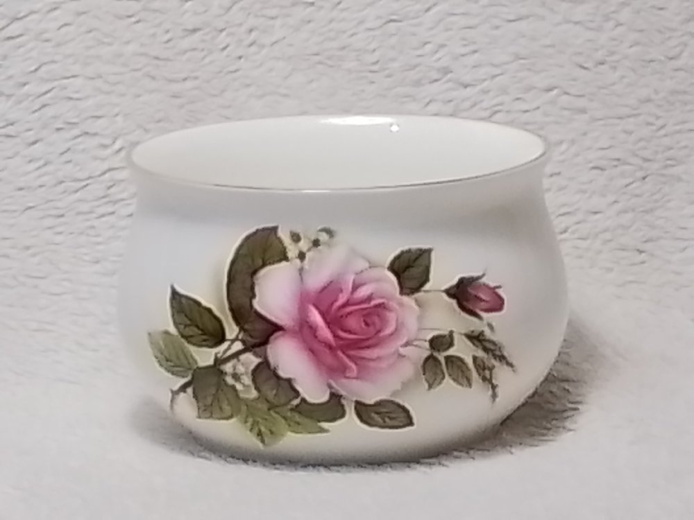 A white ceramic bowl with a pink rose and green leaves painted on it, placed on a light textured surface.