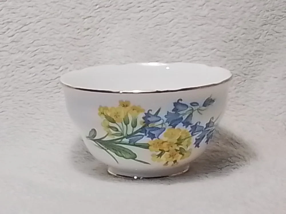 A decorative porcelain bowl with a floral pattern of yellow and blue flowers and green leaves.