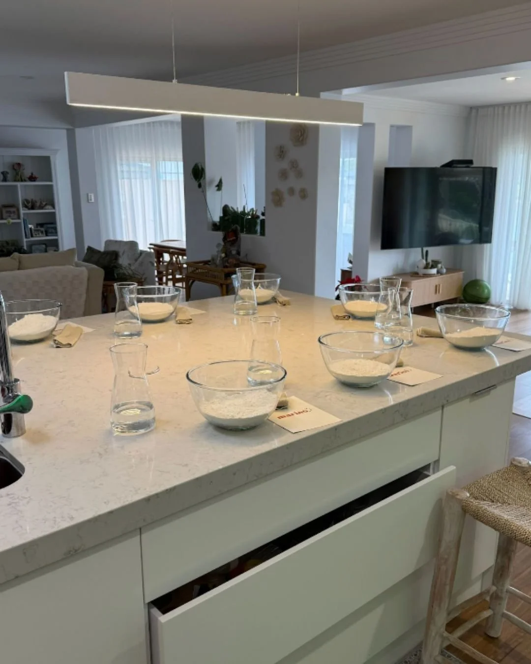 A clean kitchen island prepped for a Marino & The Dough masterclass, with individual bowls of flour, water carafes, napkins, and branded cards neatly arranged in a welcoming home setting.
