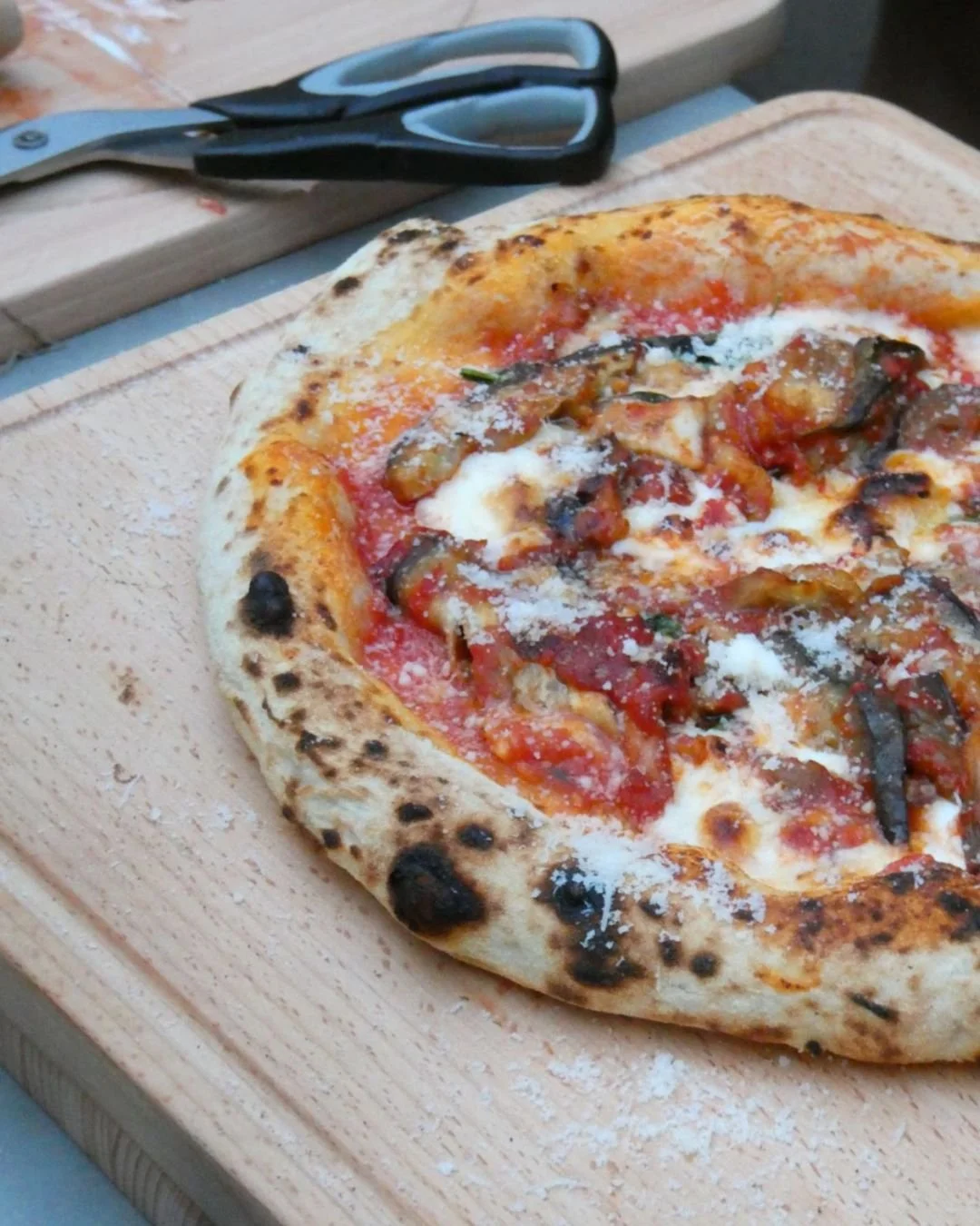 Close up of Neapolitan style pizza with blistered crust, tomato, mozzarella and parmesan on a wooden board during a Marino & The Dough masterclass