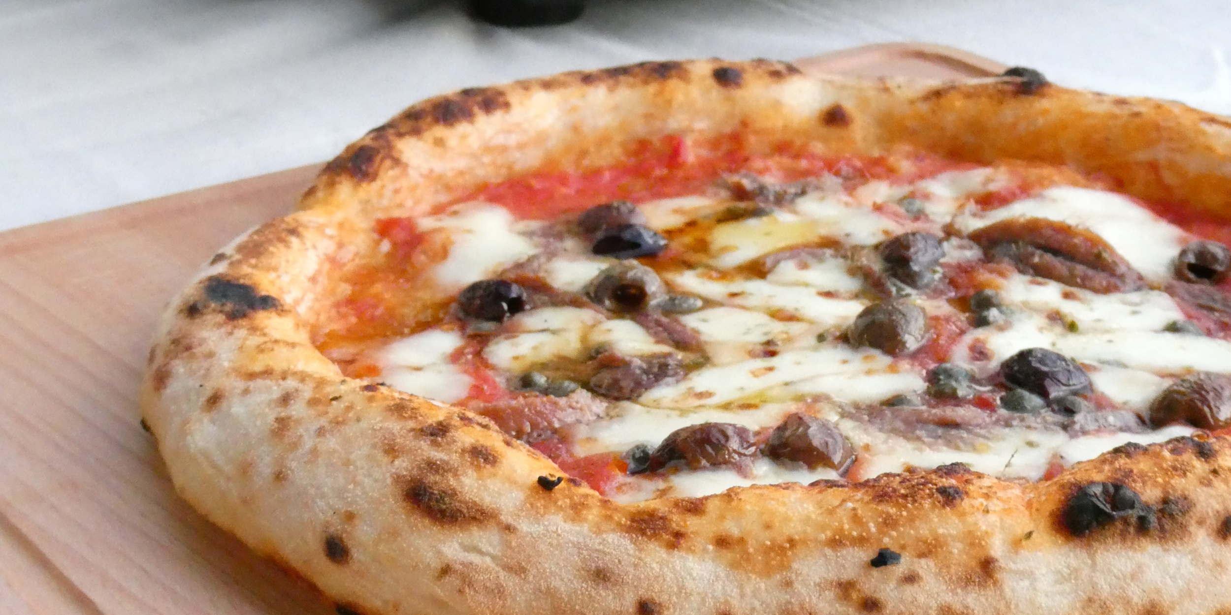 Close-up of a wood fired Neapolitan style pizza with melted mozzarella, olives and anchovies made during a Marino & The Dough masterclass