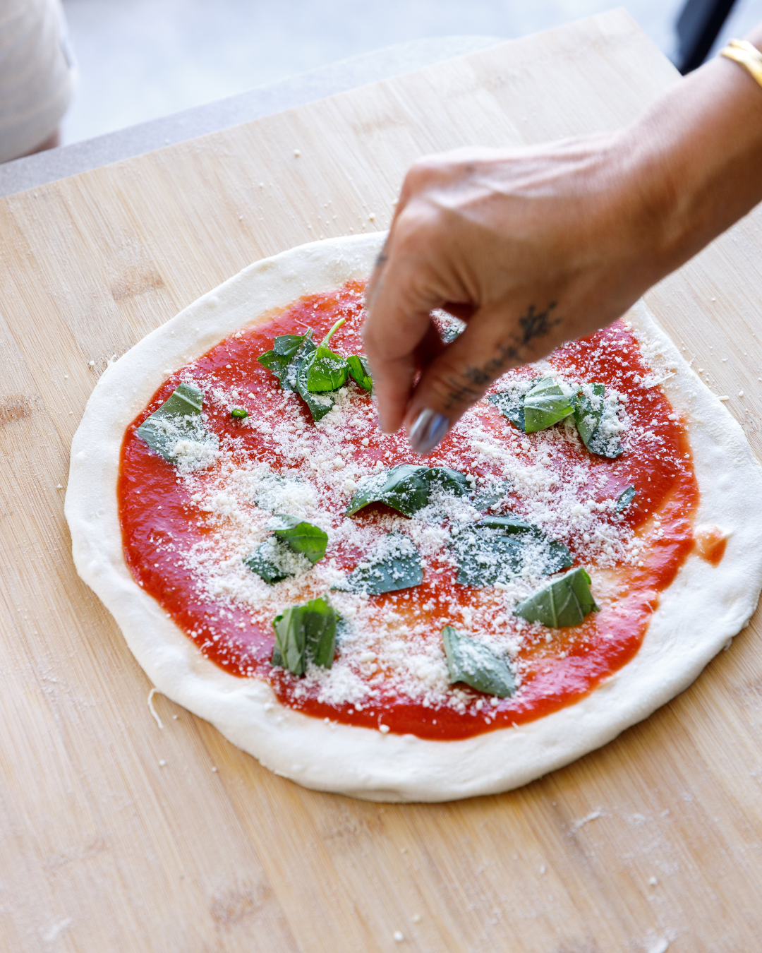 Guest adding fresh basil and grated cheese to a classic Margherita pizza during a hands on Marino & The Dough pizza making masterclass.