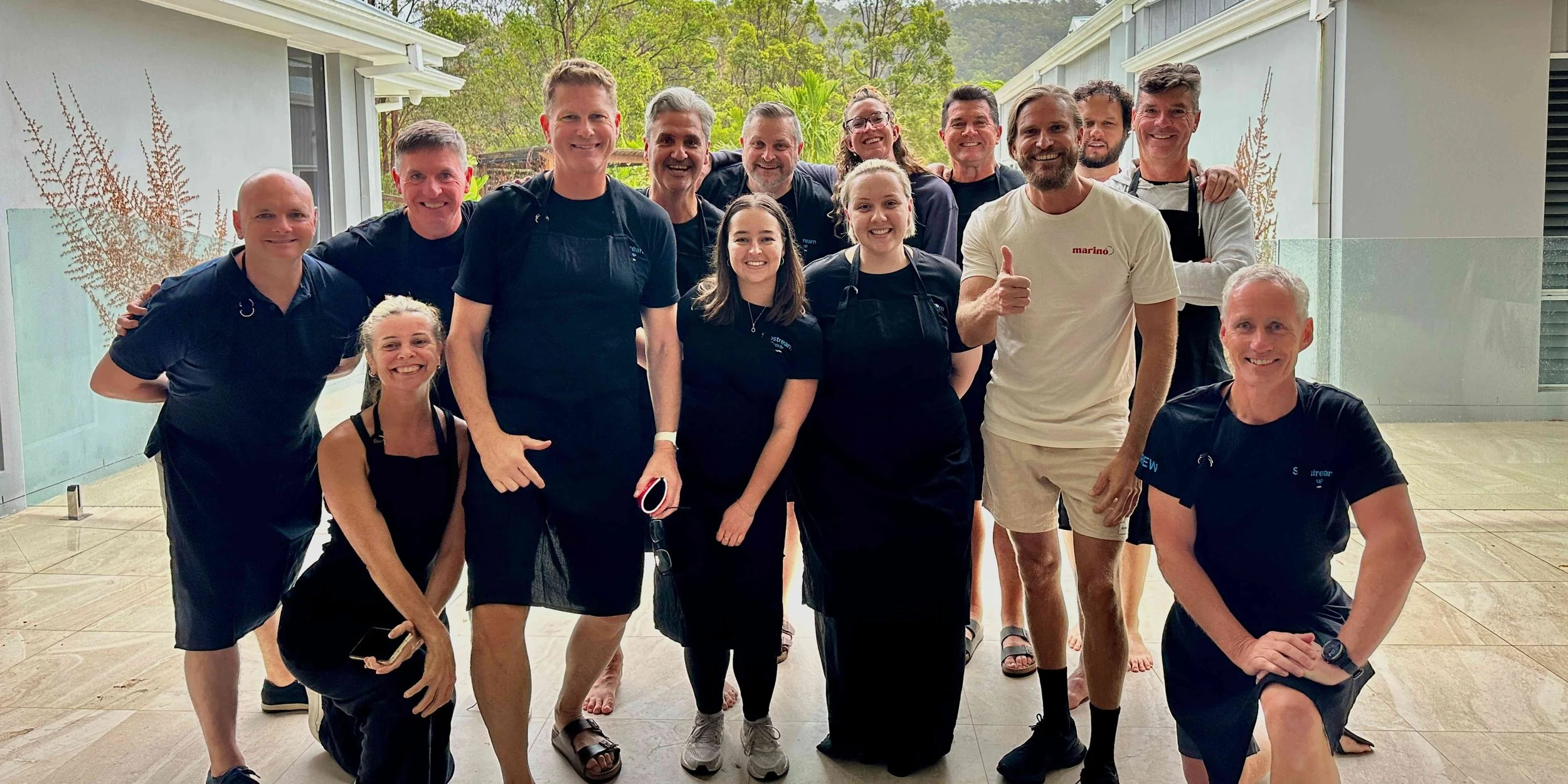 Corporate team smiling after a Marino & The Dough masterclass at a private outdoor venue, with everyone wearing aprons and relaxed post-session.
