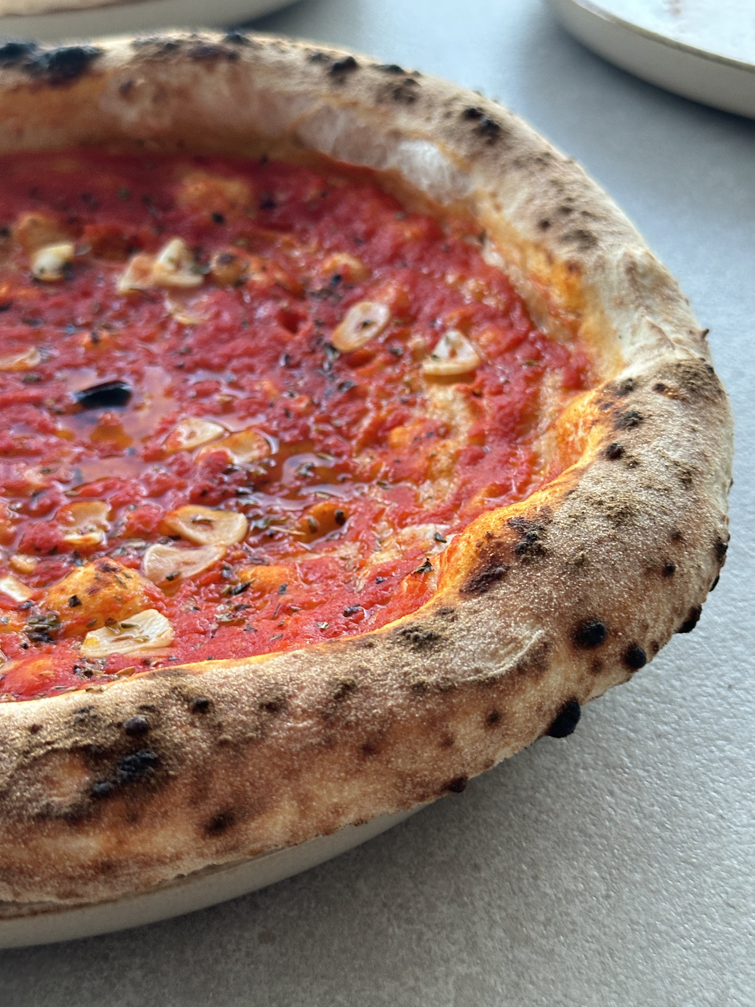 Close-up of a Neapolitan marinara pizza with tomato, sliced garlic, herbs and a blistered, airy crust.