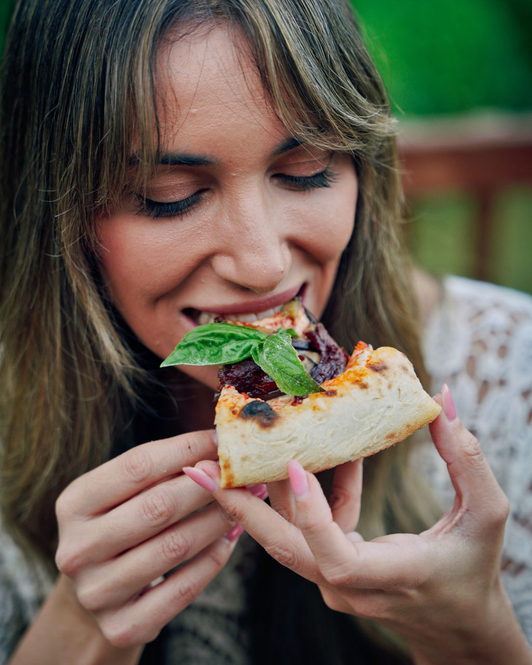 Close up of a woman taking a bite of a slice of Neapolitan style pizza with fresh basil and a thick airy crust.  I can also give you a more SEO-focused file name and alt text version for Marino & The Dough.
