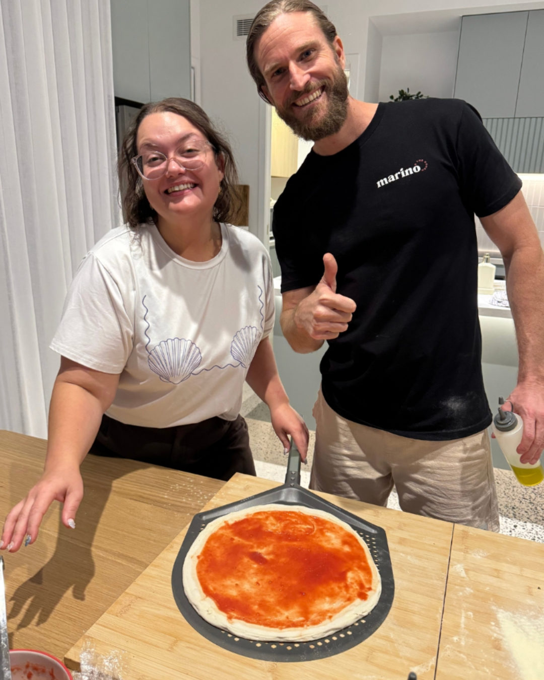 Smiling guest and pizza instructor beside a freshly shaped pizza base topped with tomato sauce during a private hen’s party masterclass.