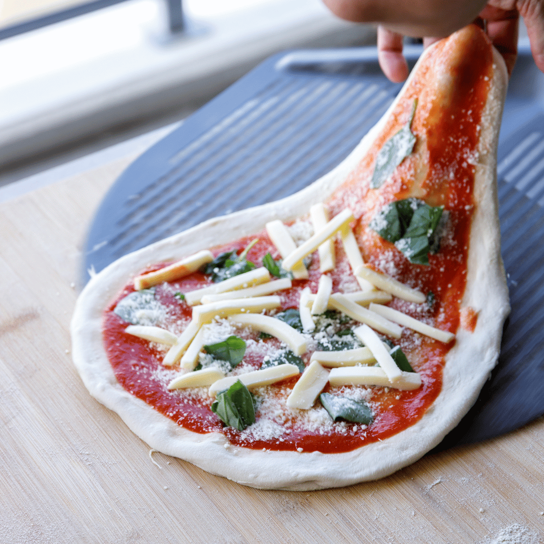 Hand stretching pizza dough topped with tomato, basil and mozzarella before baking in a high heat oven.