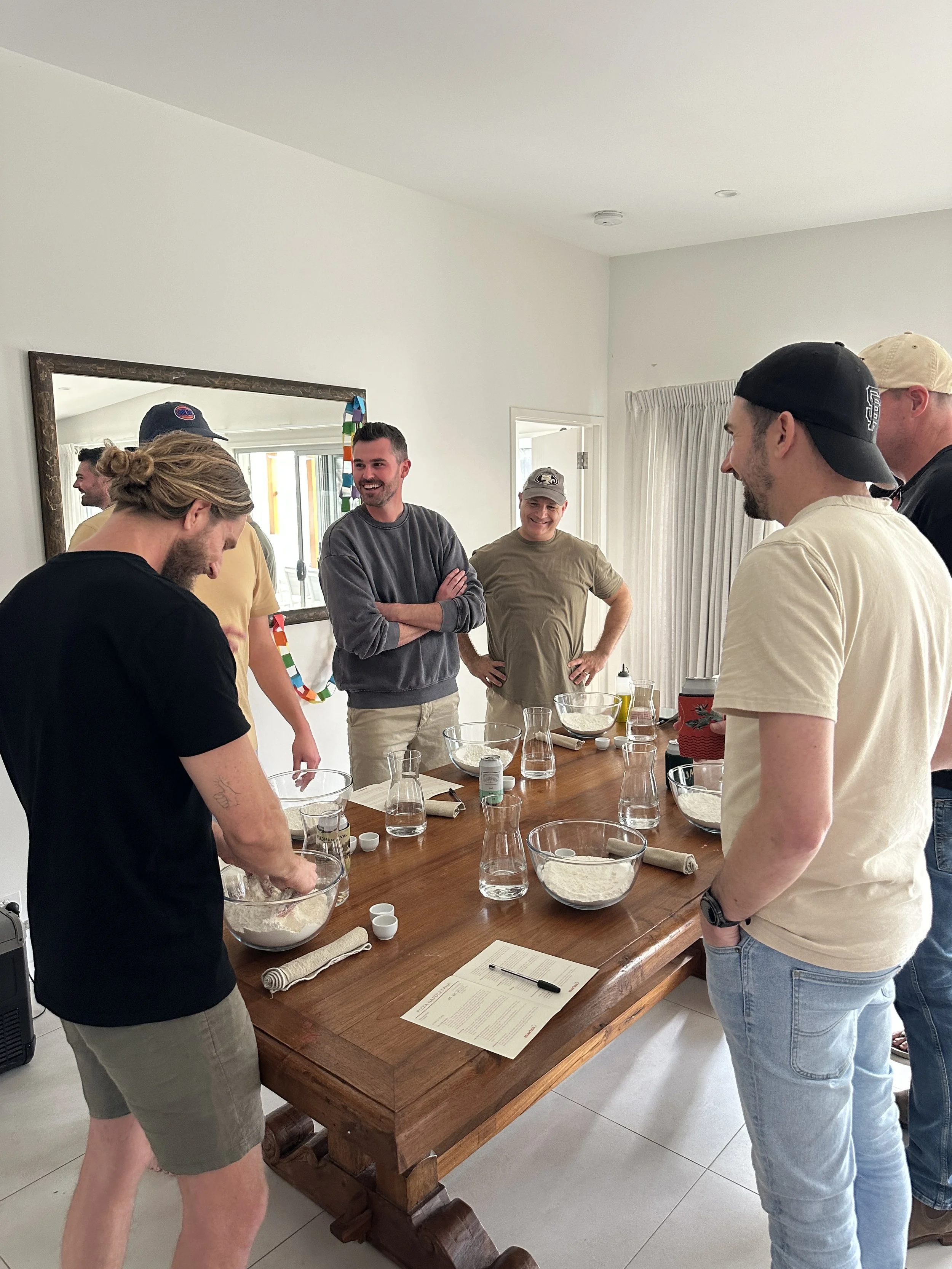 Guests kneading pizza dough at a Marino & The Dough Neapolitan pizza masterclass, gathered around a wooden table with flour bowls and recipe sheets