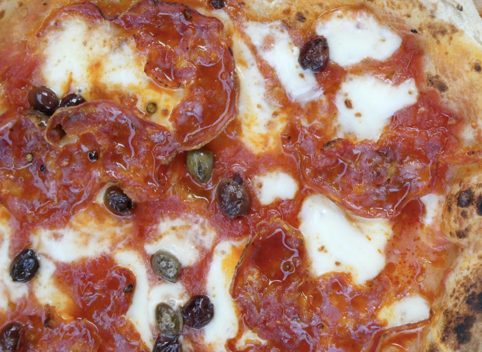 Close up of Neapolitan style pizza with salami, mozzarella, olives and rich tomato sauce, finished with olive oil during a Marino & The Dough masterclass
