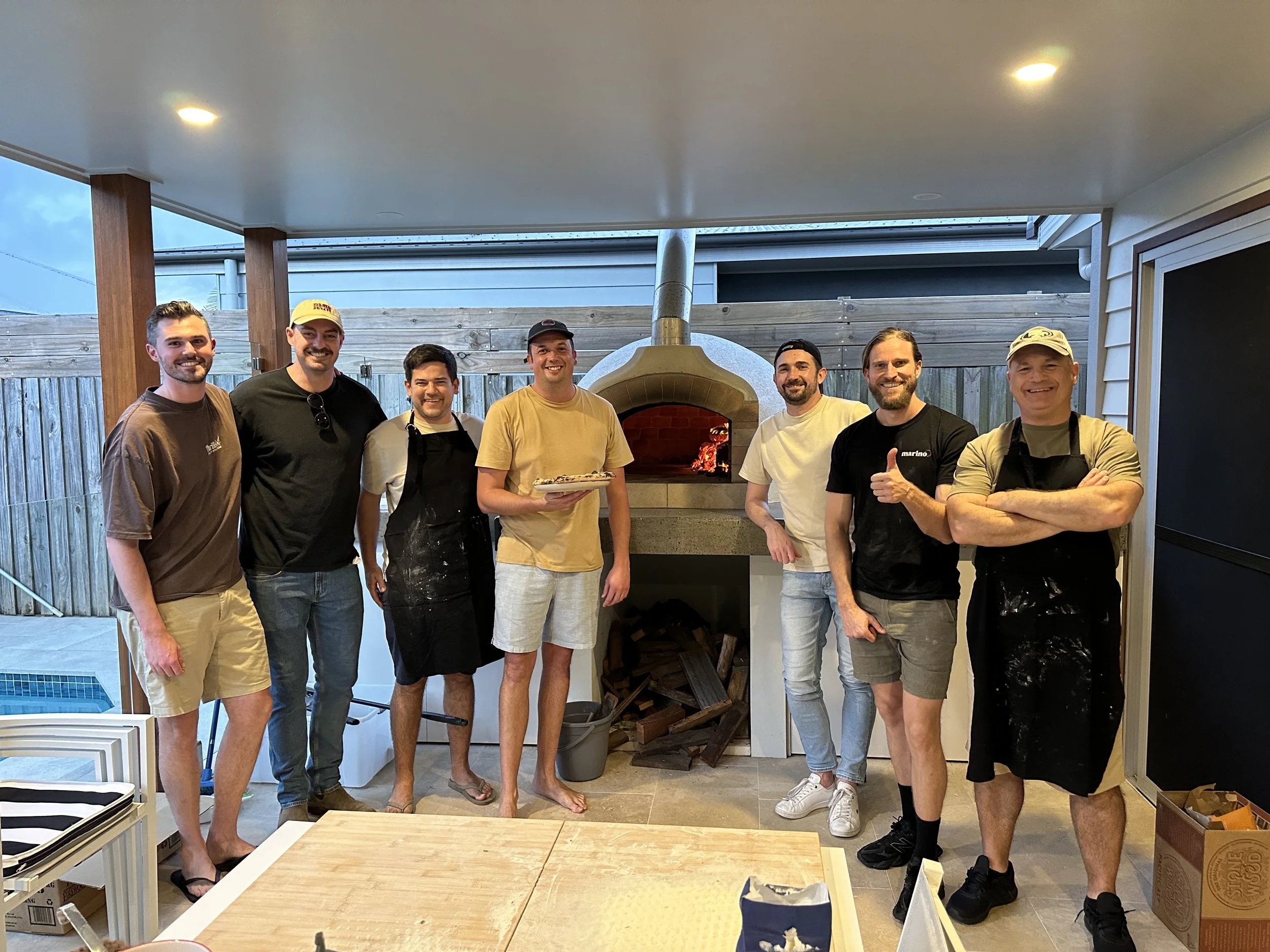 Group of masterclass guests posing in front of a wood-fired pizza oven at a Marino & The Dough Neapolitan pizza masterclass"