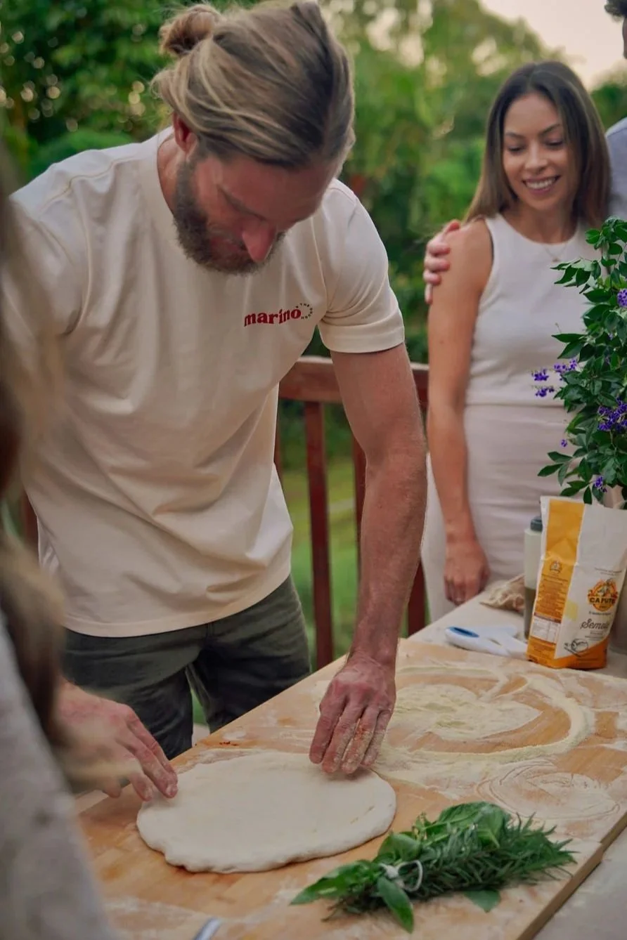 Luke Marino guiding dough stretching during a private pizza masterclass on the Gold Coast, with guests observing in an outdoor home setting.