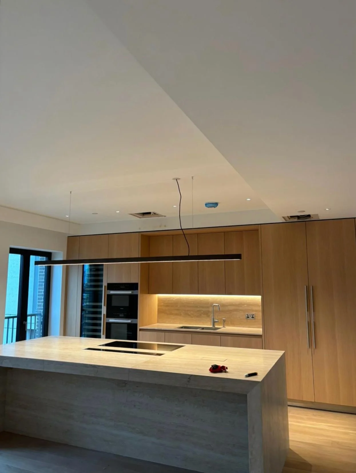 Modern kitchen with marble island, built-in ovens, wooden cabinets, and under-cabinet lighting.