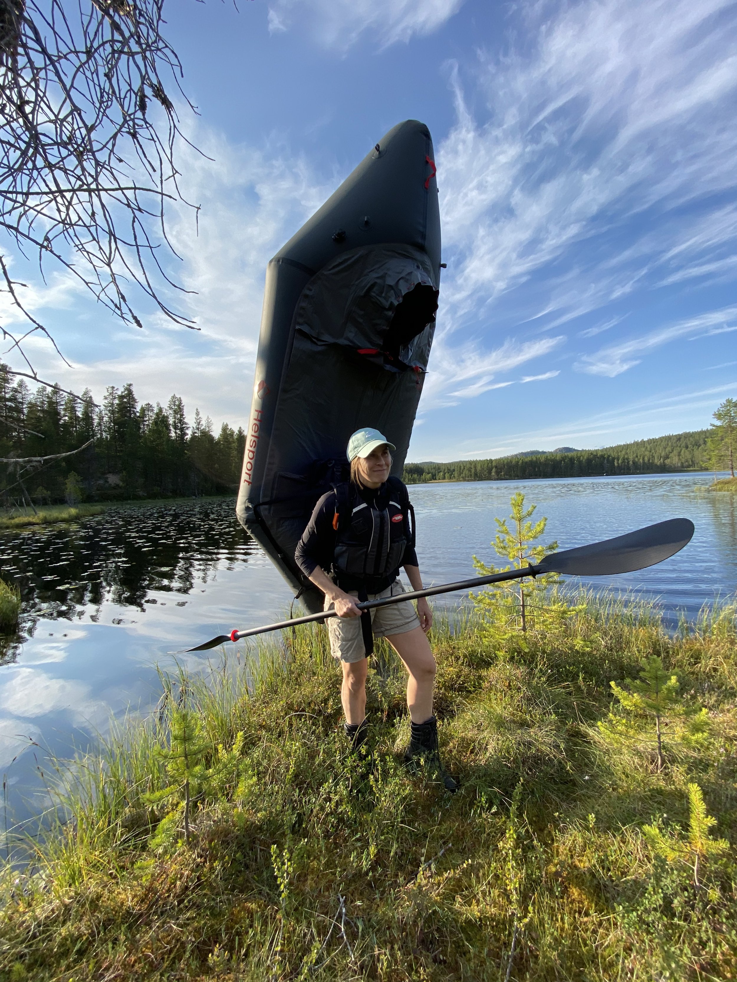 Person som holder en oppblåsbar bil packraft på ryggen ved en innsjø