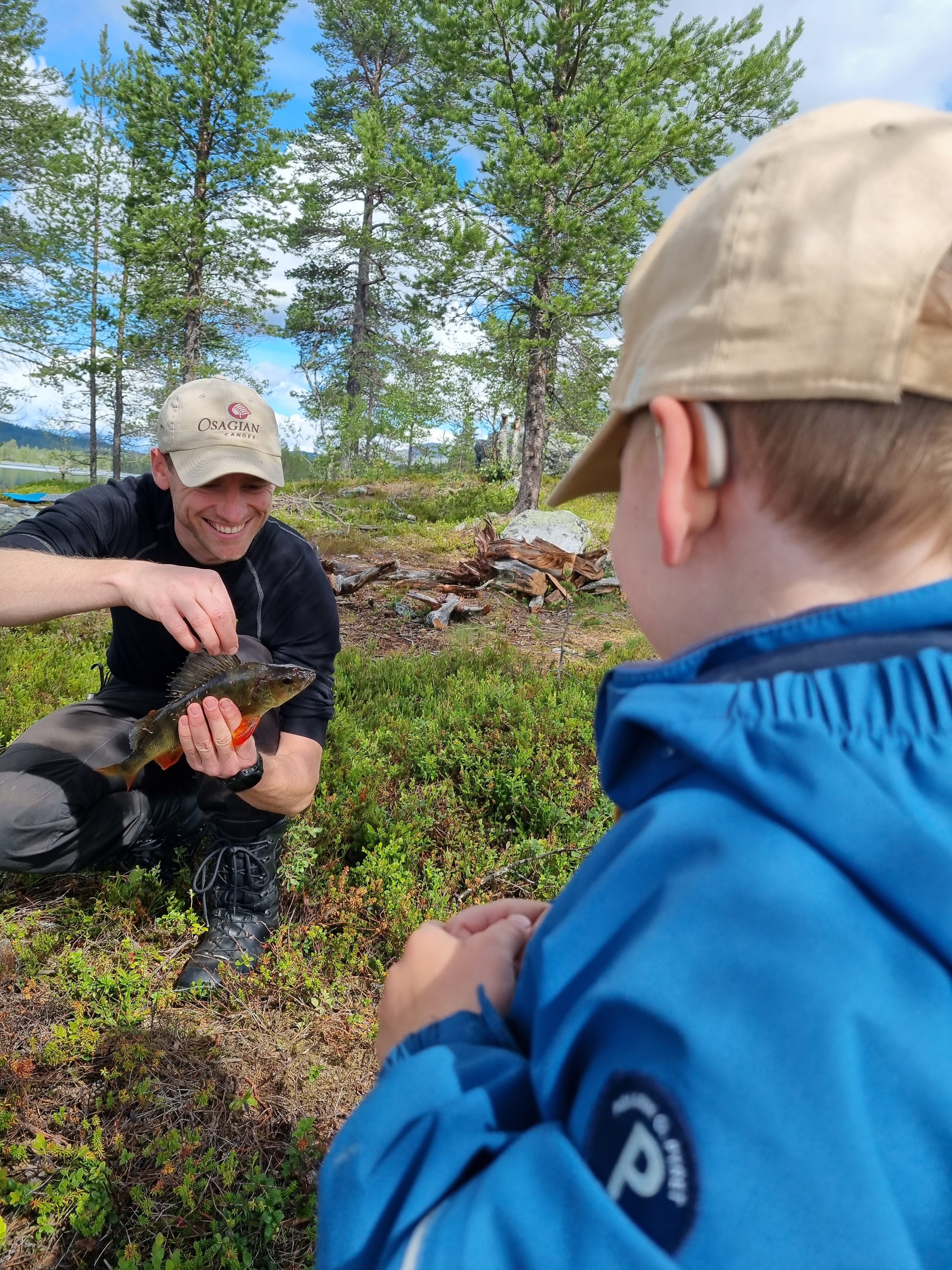 Man holding a fish with a child watching in a forest setting
