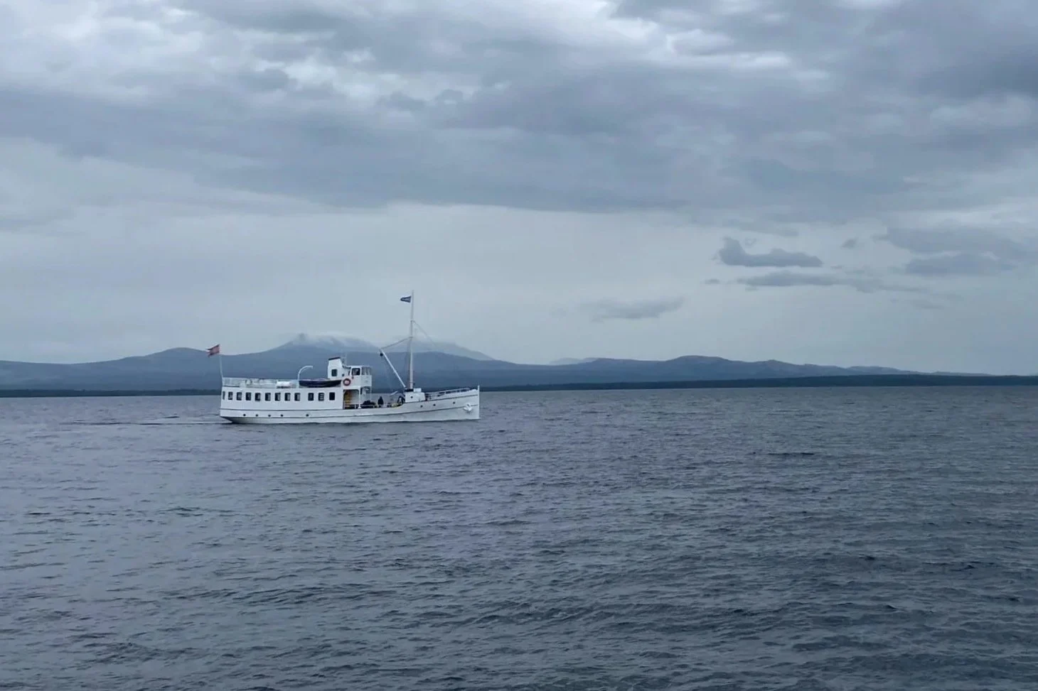 A white boat sailing in calm waters during overcast weather with mountains visible in the background.