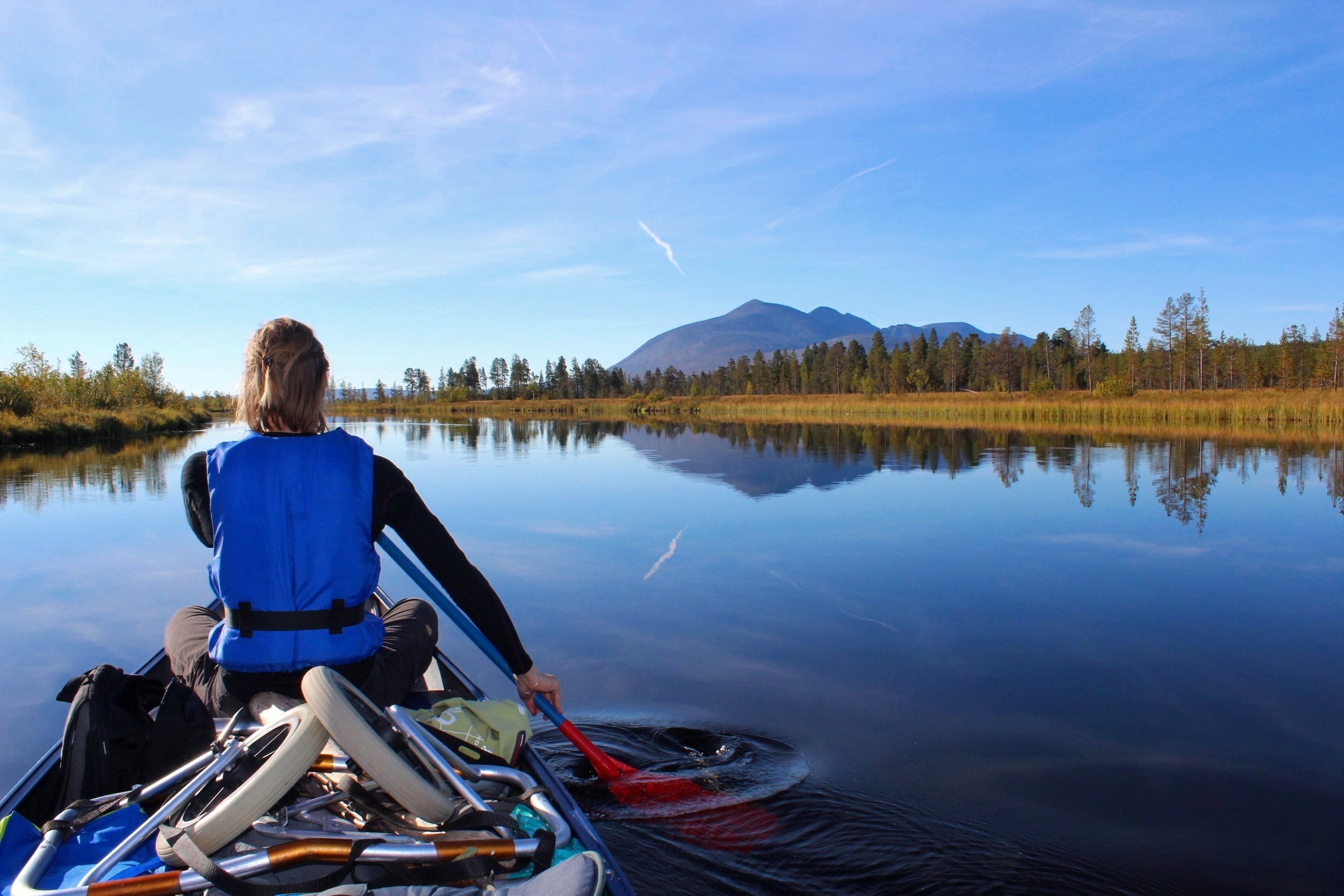 Person kayaking on a calm lake with mountain and forest in the background on a clear day.